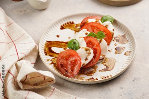 Traditional italian salad caprese consisting of slices red tomatoes, fresh basil and mozzarella cheese with balsamic vinegar dressing on concrete background, wooden pepper and salt mills