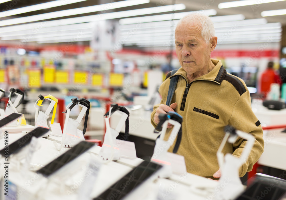 Fototapeta premium elderly grayhaired man pensioner examining counter with electronic gadgets and smart watches in showroom of digital goods store