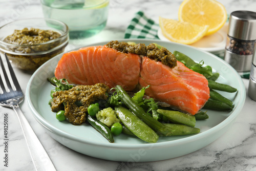 Tasty cooked salmon with pesto sauce and fresh salad served on white marble table