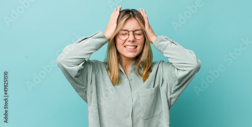 young pretty blonde woman feeling stressed and anxious, depressed and frustrated with a headache, raising both hands to head photo
