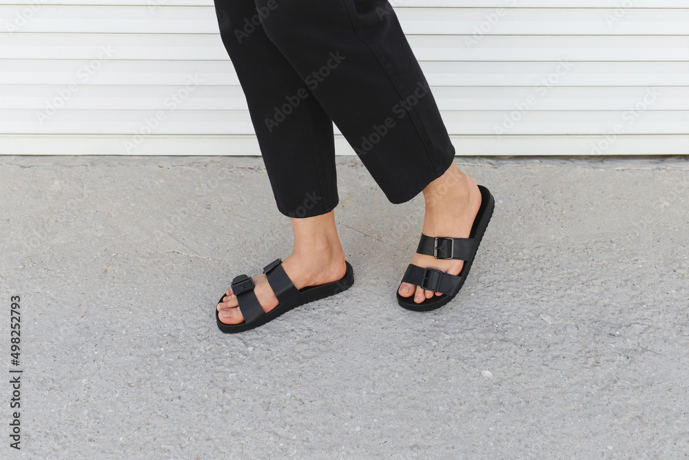 Women's legs in black flat sandals. Trendy female footwear. Summer women's  shoes. Details of stylish basic minimalistic casual outfit. Street fashion.  No face. Photos | Adobe Stock