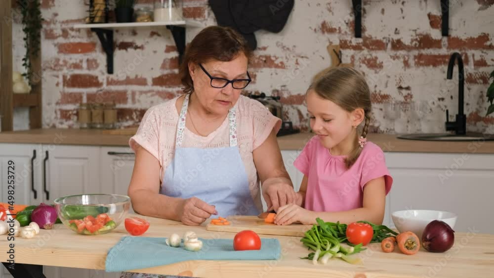 Grandmother Teaching her Cute Little Granddaughter Cutting Carrot in the Kitchen. Eco-friendly Products for Cooking and Healthy Vegan Eating Concept Grandmother Teaching her Cute Little Granddaughter Cutting Carrot in the Kitchen. Eco-friendly Products for Cooking and Healthy Vegan Eating Concept