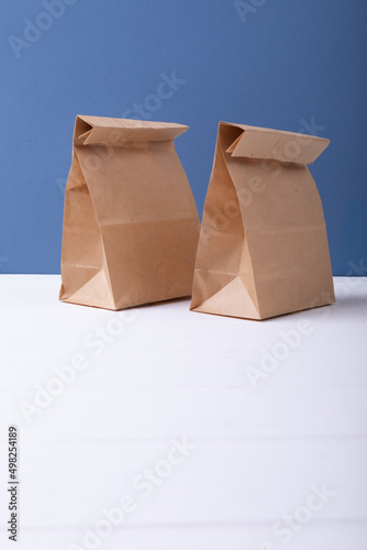 Two paper lunch bags on white surface with copy space on blue background