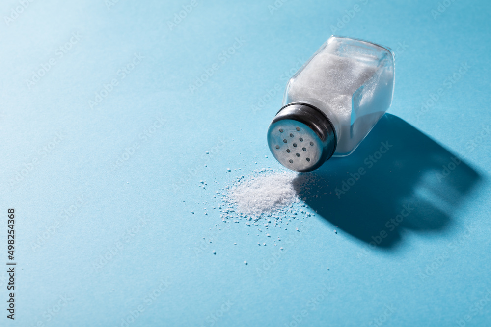 High angle close-up of salt spilling from salt shaker on blue background with copy space High angle close-up of salt spilling from salt shaker on blue background with copy space