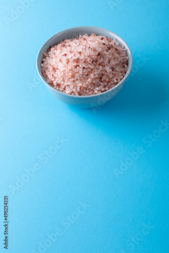 Close-up of pink rock salt in bowl over blue background with copy space