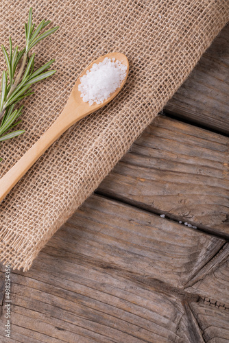 Close-up of white rock salt in wooden spoon by rosemary on jute fabric at table