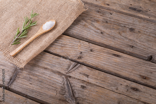 High angle view of rock salt in wooden spoon and rosemary on jute fabric at table with blank space
