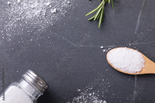 Directly above shot of salt with salt shaker, spoon and rosemary on table