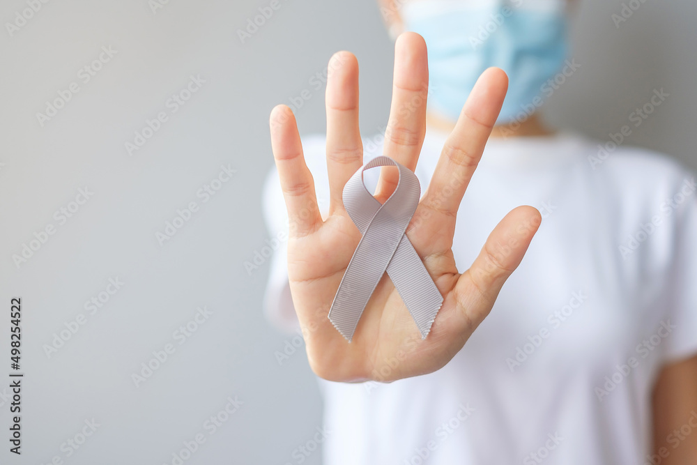 Naklejka premium Brain Cancer Awareness month, woman hand holding grey color Ribbon for supporting people living. Healthcare and World cancer day concept