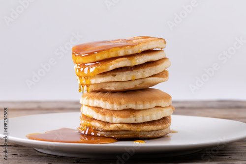 Stack of eight pancakes with syrup served in plate on table against gray background