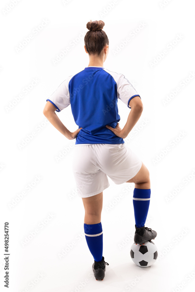 Rear view of biracial young female player with hand on hip standing on soccer ball Rear view of biracial young female player with hand on hip standing on soccer ball