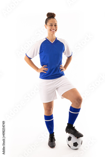 Portrait of smiling biracial young female player with hand on hip and foot on soccer ball