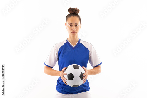 Portrait of biracial young female player holding soccer ball while standing against white background