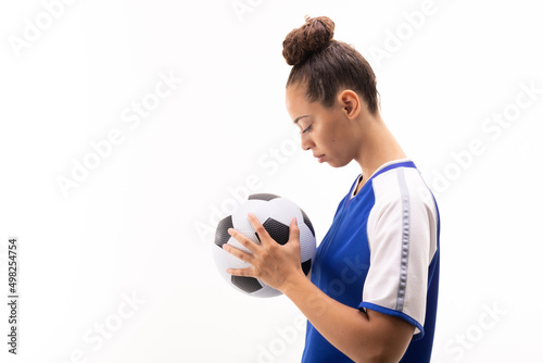 Side view of biracial young female soccer player looking at soccer ball against white background