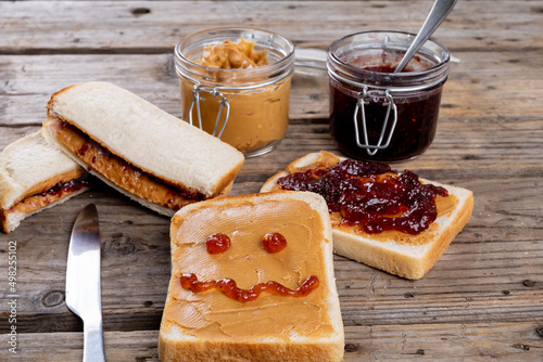 Anthropomorphic face made with jam on bread with peanut butter by sandwiches and jars on table