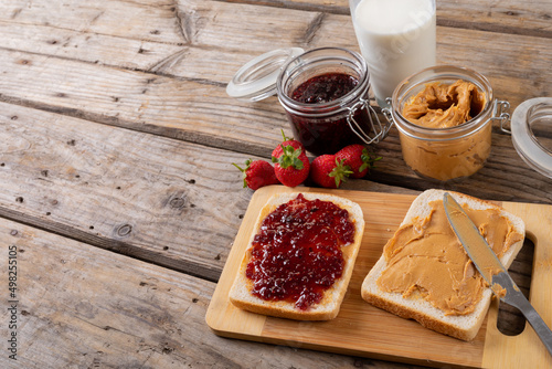 Peanut butter and jelly sandwich on serving board with jars, strawberries and milk at table