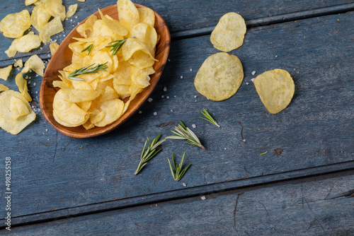 High angle view of potato chips in bowl with rosemary and salt on wooden table
