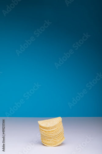 Stacked potato chips on table against blue background with copy space