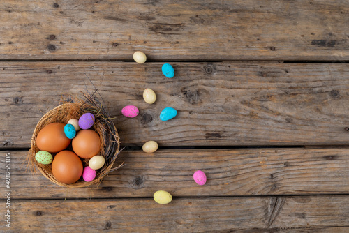 Directly above shot easter eggs and colorful candies in nest on wooden table