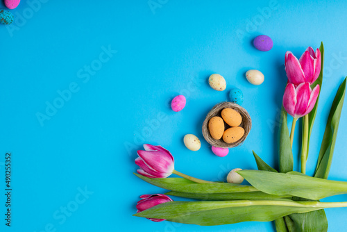 Directly above shot of easter candies in small nest with pink tulips on blue background