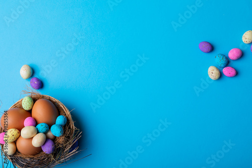 Easter eggs with colorful candies in nest on blue background with copy space