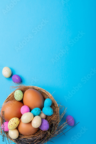 Directly above shot of easter eggs with colorful candies in nest on blue background with copy space