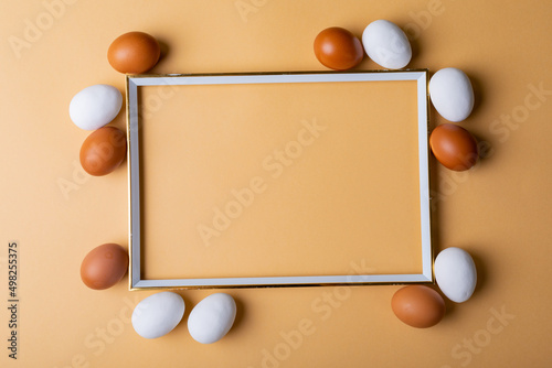 Overhead view of easter eggs around empty frame on orange background with copy space