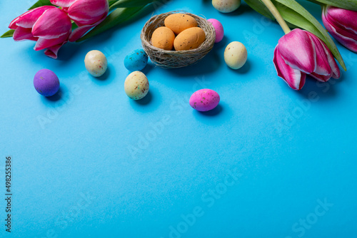 High angle view of easter candies in small nest with pink tulips on blue background with copy space