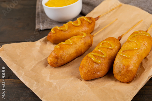 Corn dogs served with mustered sauce on paper bag at table