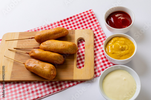 High angle view of corn dogs on serving board with various savory sauces in bowl on table