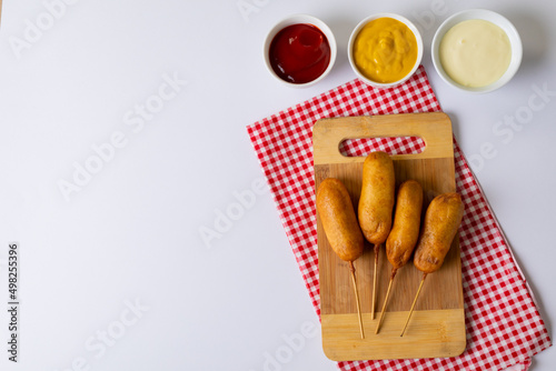 Overhead view of corn dogs on serving board with various savory sauces in bowl on table