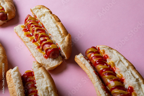 High angle view of yellow and red sauces on hot dogs over pink background