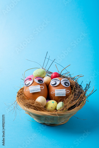 Easter eggs with doodle eyes and mask with candies and straws in nest on blue background
