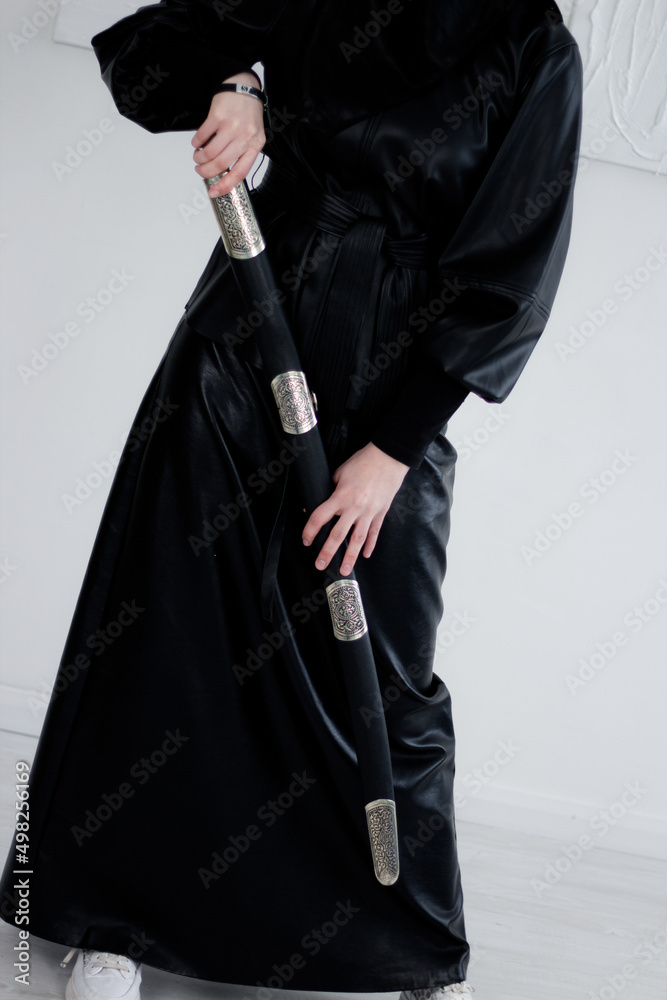 Woman in hijab, black headscarf and dress. The woman is holding a sword in her hand. Stylish young beautiful Muslim woman. Woman in hijab, black headscarf and dress. The woman is holding a sword in her hand. Stylish young beautiful Muslim woman.