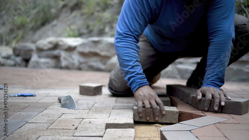 Closeup of hand putting brick paver into place in a hardscaping project.