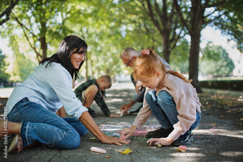 Slika na platnu Senior couple with grandchildren drawing with chalks on pavement outdoors in park