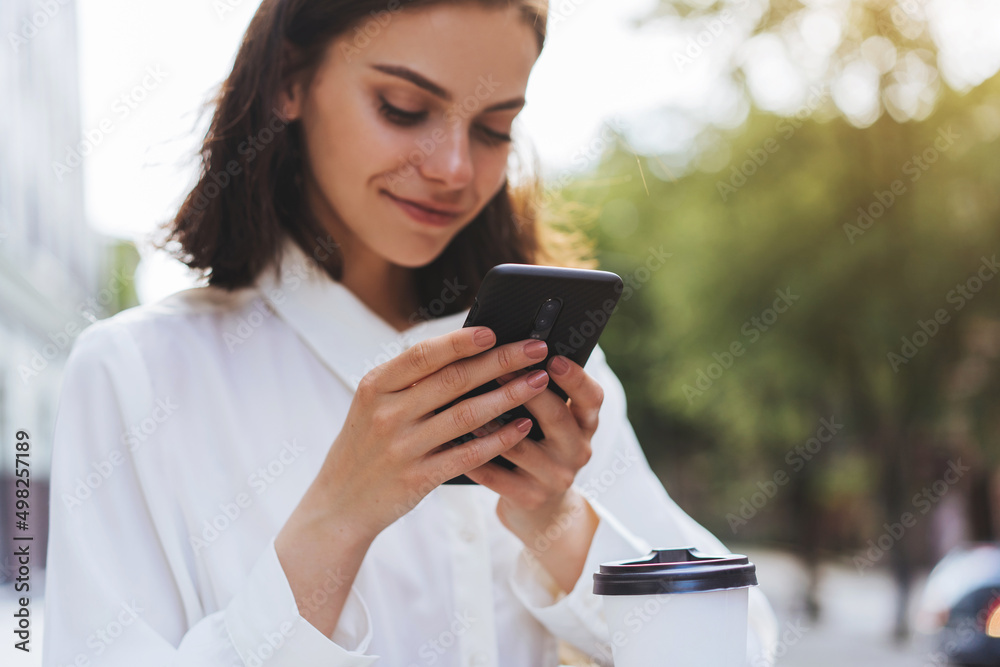 Close up of hands using cell phone with background of the city, smiling girl texting with friends while walking outdoor Close up of hands using cell phone with background of the city, smiling girl texting with friends while walking outdoor
