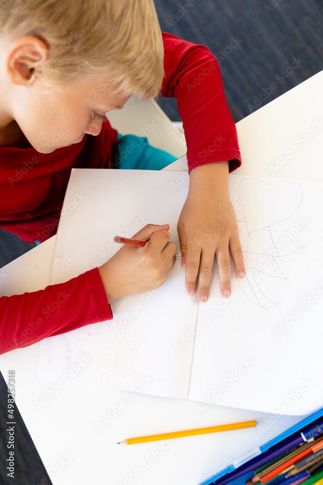 High angle view of caucasian elementary schoolboy writing on book while sitting at desk in school High angle view of caucasian elementary schoolboy writing on book while sitting at desk in school