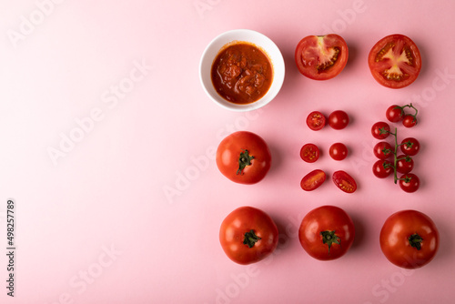 Overhead view of fresh puree in bowl by various red tomatoes by copy space on pink background