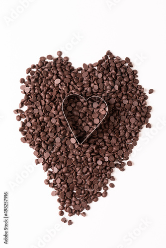 Overhead view of heart shape pastry cutter over chocolate chips on white background