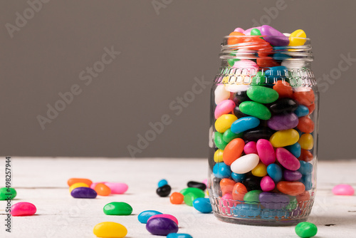 Close-up of full glass jar with multi colored candies against gray background with copy space