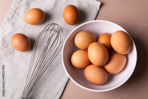 Directly above view of fresh brown eggs in bowl by wire whisk on napkin over table
