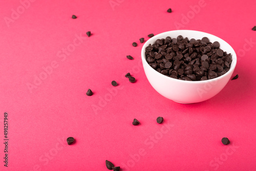 High angle view of fresh chocolate chips full of white bowl against pink background