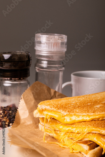 Close-up of fresh cheese sandwich on wax paper by peppercorn bottle and cup against gray background