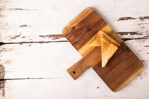 Overhead view of fresh fresh cheese sandwich on wooden serving board over white table
