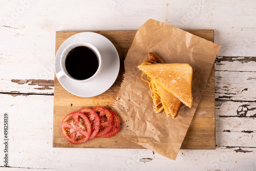 Overhead view of fresh cheese sandwich with tomato slices and black coffee on serving board