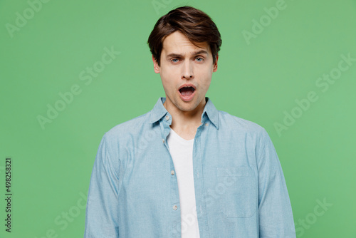 Tired upset young brunet man 20s years old wears blue shirt did not get enough sleep last night after party and barely got up in the morning yawning isolated on plain green background studio portrait.