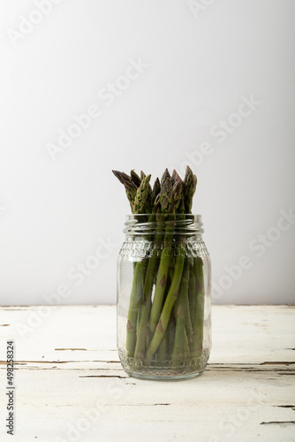 Raw green asparagus vegetables in glass jar on table against gray background with copy space