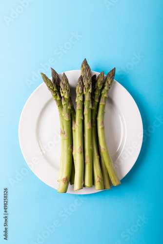 Directly above view of green raw asparagus in white plate over blue background