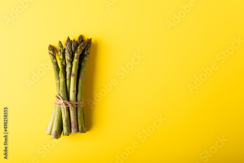 Directly above view of string tied raw asparagus bunch by copy space against yellow background